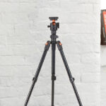 Kenro Karoo Compact Travel Tripod Kit set up in a bright indoor setting, standing on a white floor against a white brick wall, with photography books in the background.