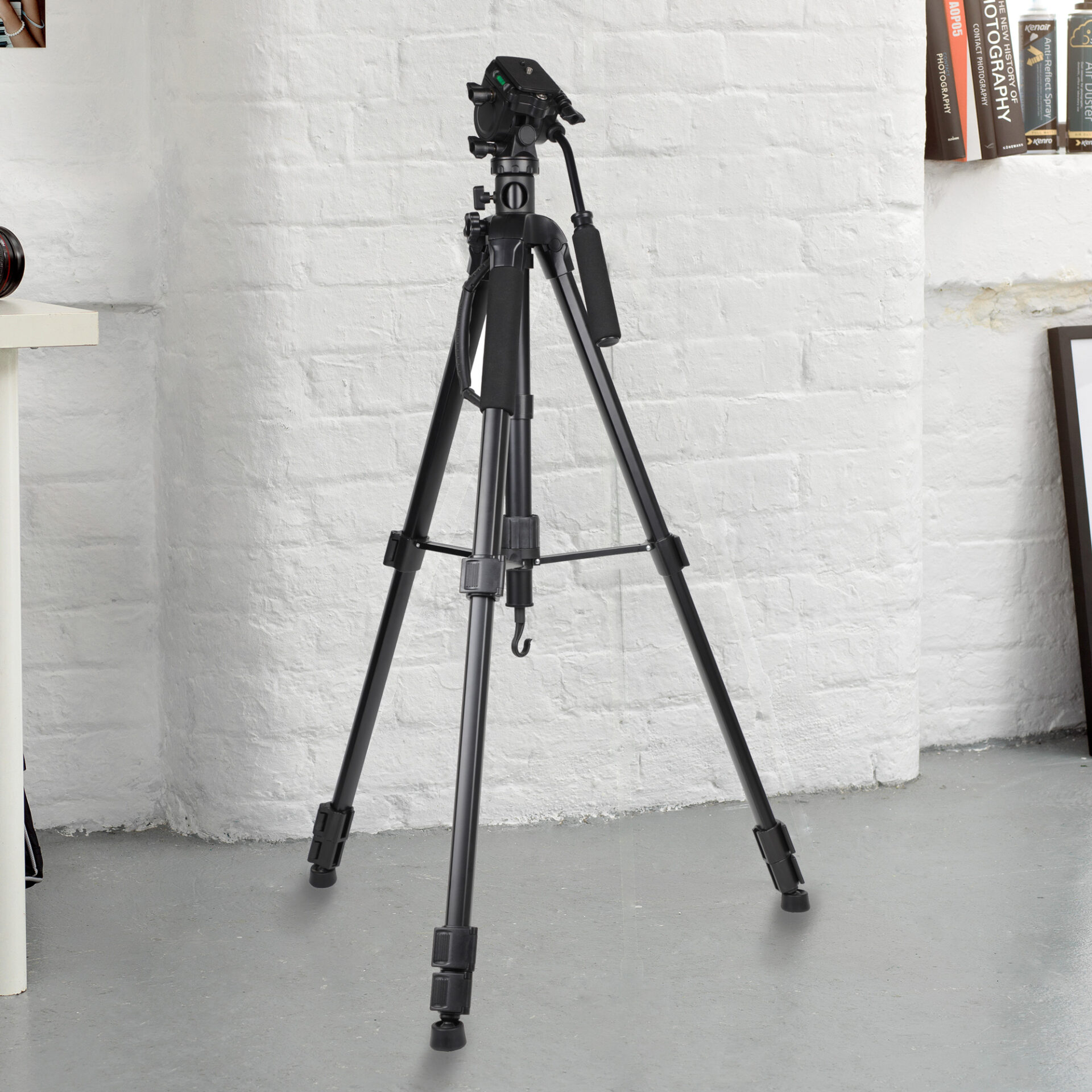 Kenro Karoo Photo & Video Tripod Kit fully extended on a white floor against a white brick wall, highlighting its tall stature and sturdy leg design for professional use.