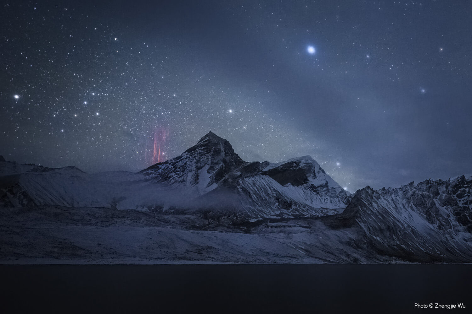 A night sky glittering with stars over mountainous terrain, with the rare red sprite lightning phenomenon visible above the peaks, adding a touch of mystery to the scene.