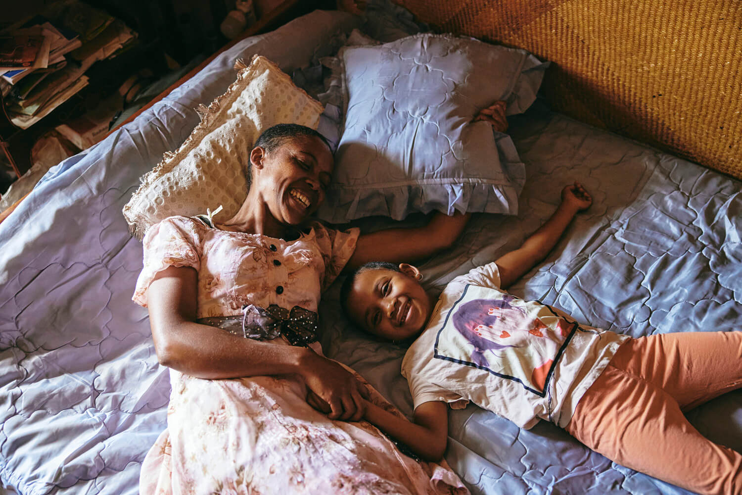 A woman and a young child lying on a bed, laughing and holding hands, showcasing a moment of joy and familial love.