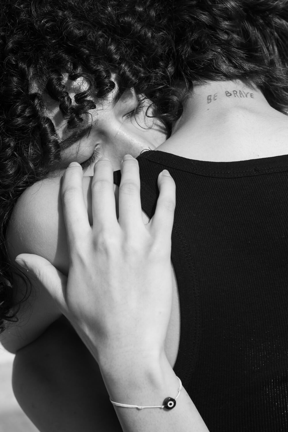 Two individuals in a close embrace, one with curly hair and a tattoo on their neck that reads 