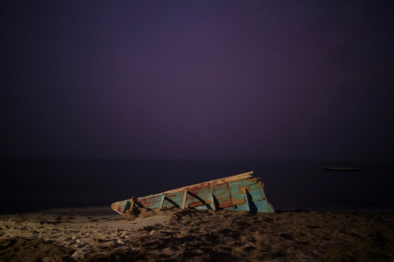 A derelict boat rests on a sandy beach under a twilight sky, symbolizing stillness and abandonment in a marine landscape.
