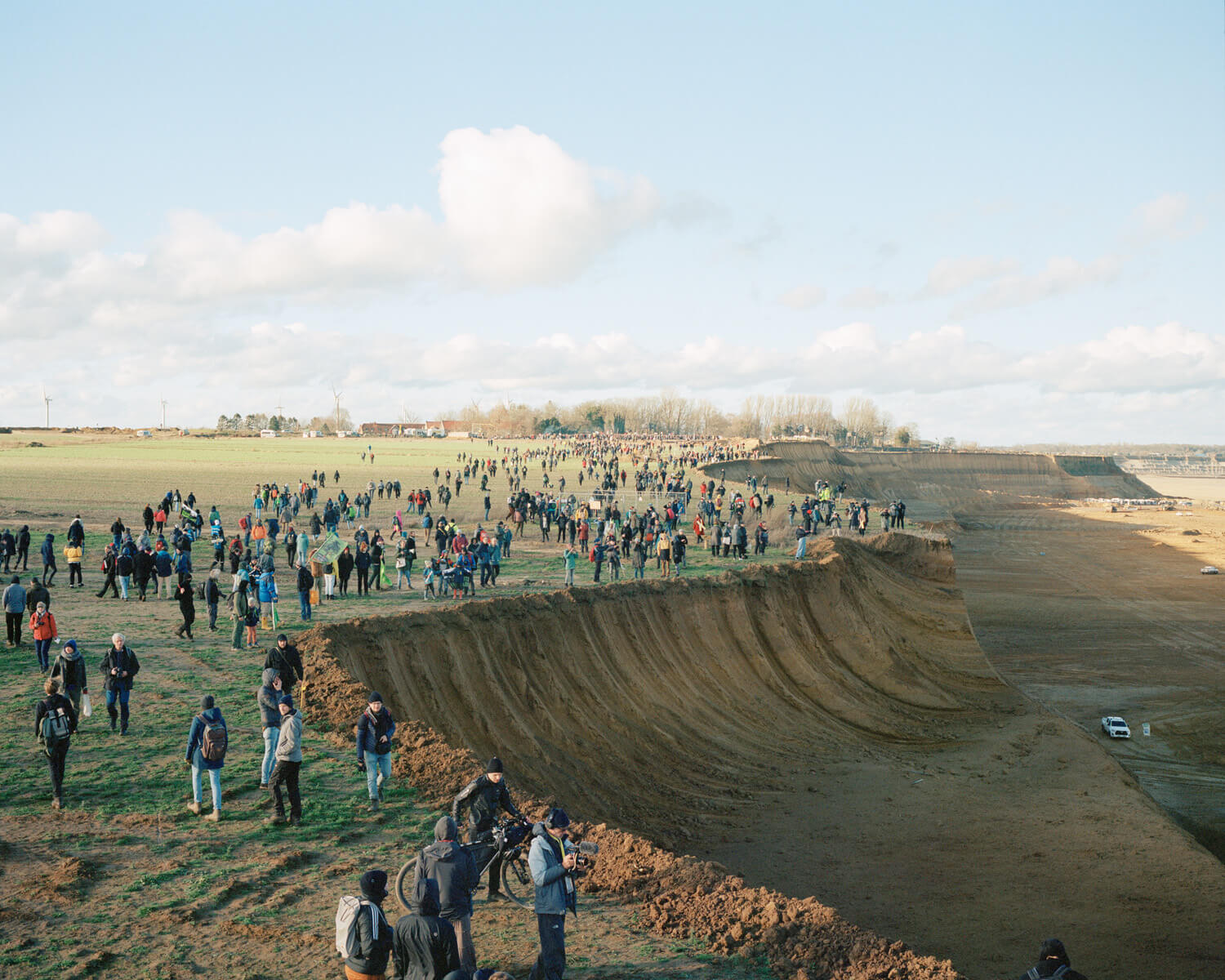 A crowd of people gathered at the edge of a quarry site that has carved away the rural landscape.