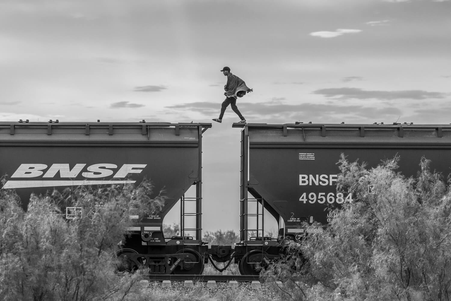 A man steps across the gap between freight train carts as he walks along the top of a train