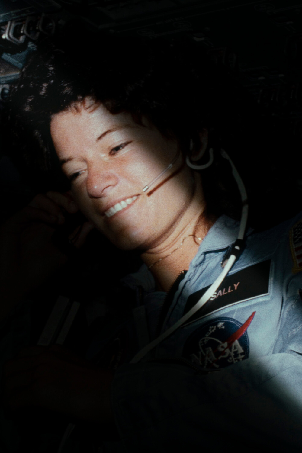 An astronaut in a space shuttle, illuminated by a shaft of light, converses on a headset, epitomizing human achievement and exploration.