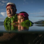 An elder and a child, half-submerged in water, in a portrait of resilience and adaptation in a changing climate.