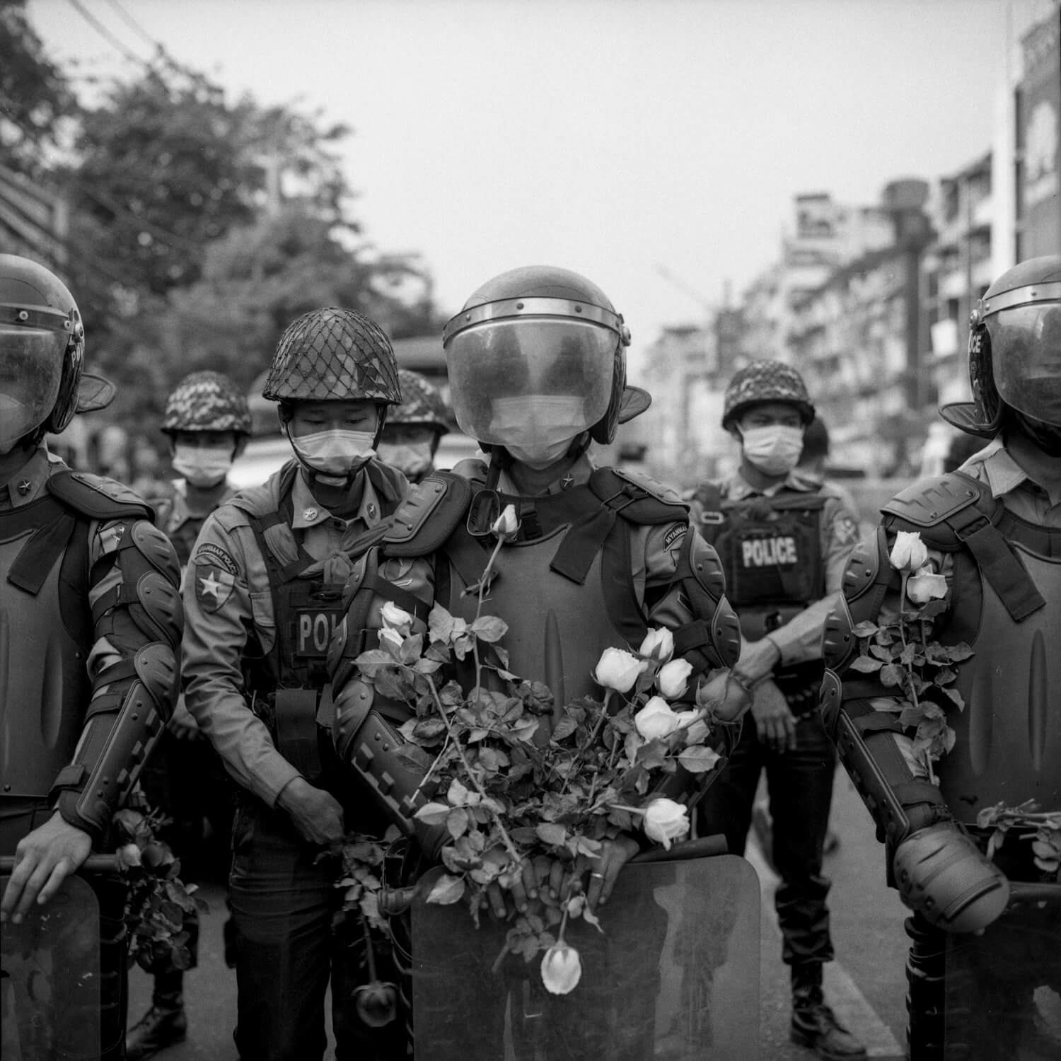 A policeman in riot gear is covered in roses apparently placed upon his person by protestors.