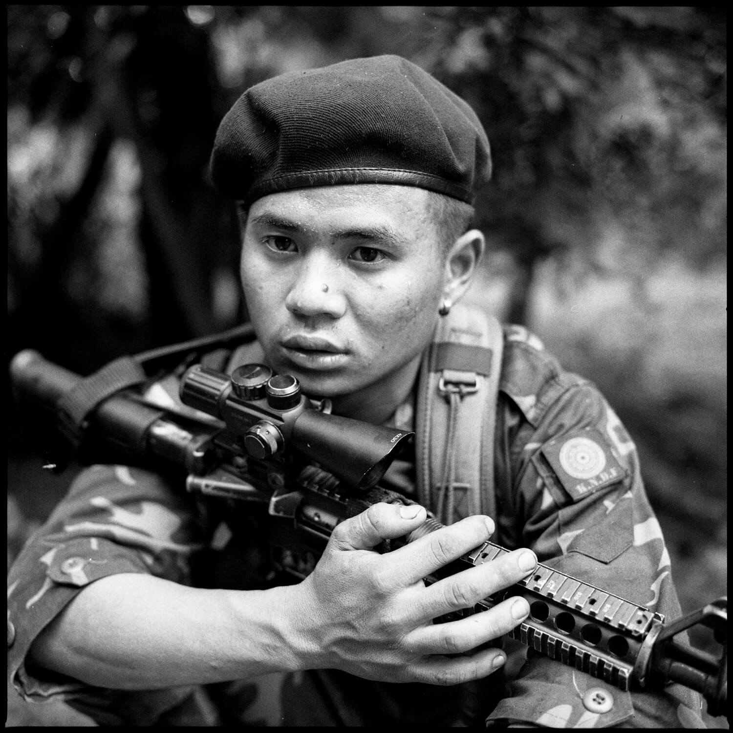 A soldier stares with a look of shocked reflection while clutching an automatic rifle across his chest.