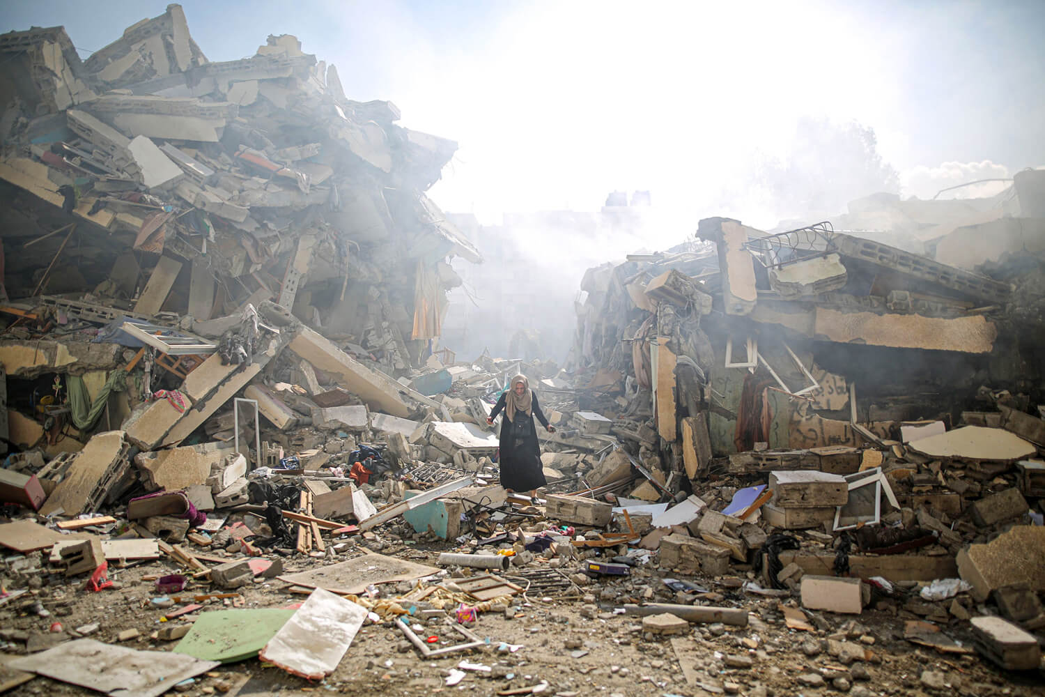 A woman stands among rubble in what was once a street surrounded by buildings.